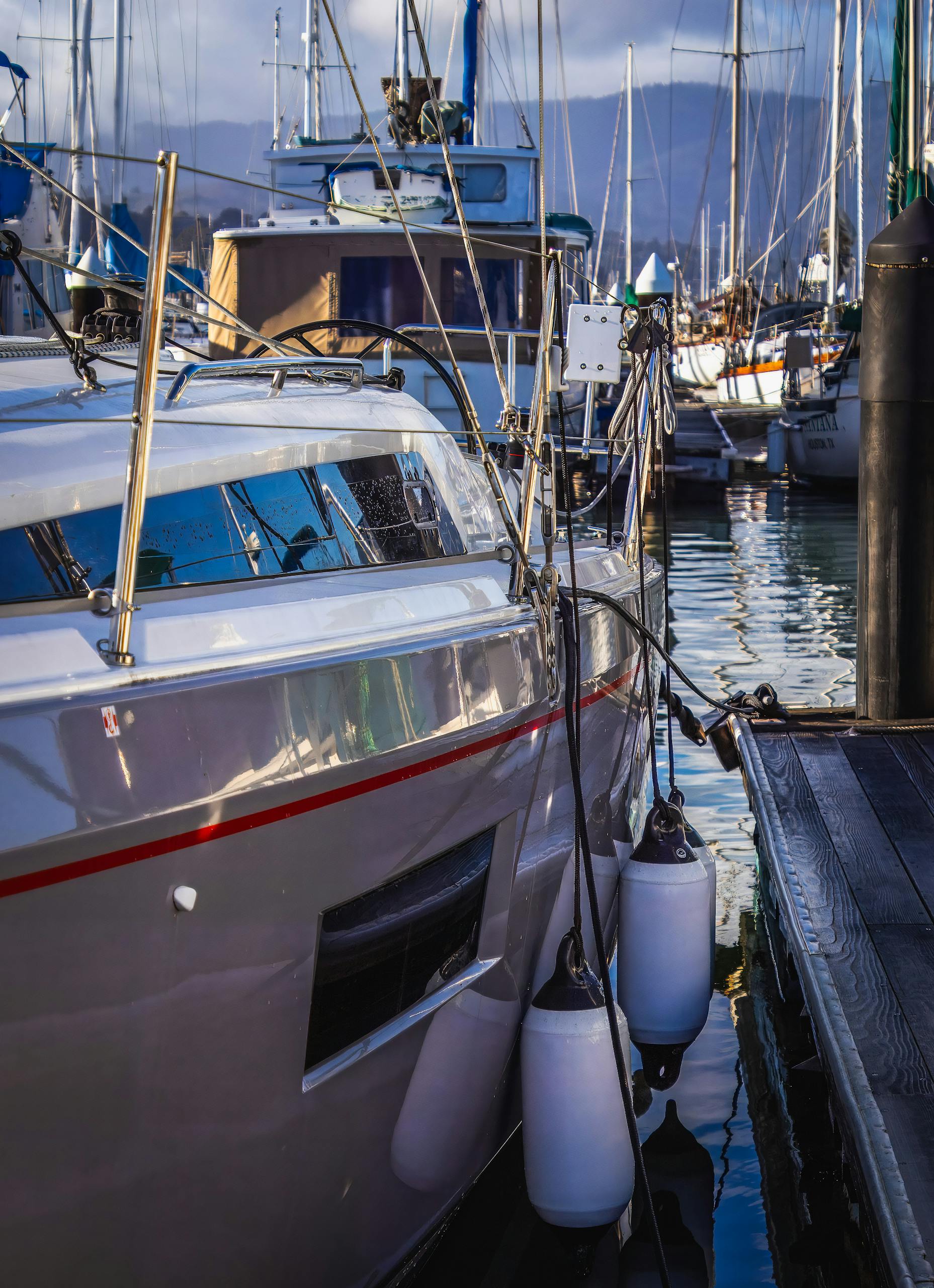 Close-up of a sleek sailboat docked at a marina, reflecting on tranquil waters.